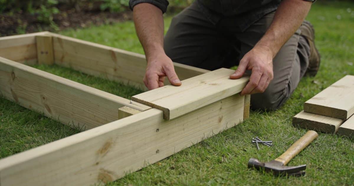 Homme agenouille assemble planches de bois en jardiniere